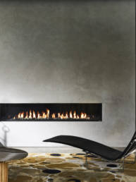 Fireplace built in the wall which has a grey background with the mustard rug on the floor along side a black resting chair