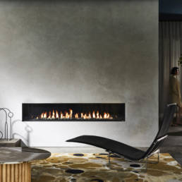 Fireplace built in the wall which has a grey background with the mustard rug on the floor along side a black resting chair